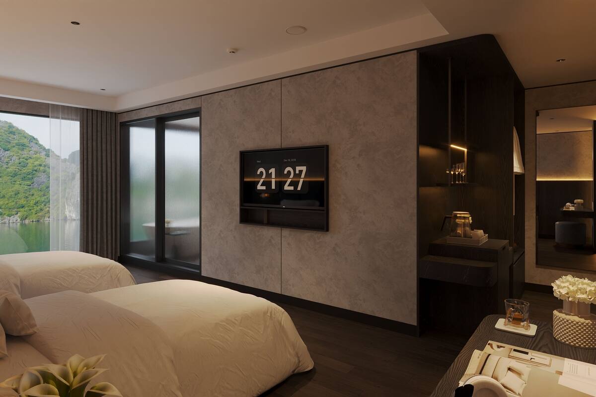 A modern hotel room with a large window, a digital clock, a bed, a desk, and a bathroom area.