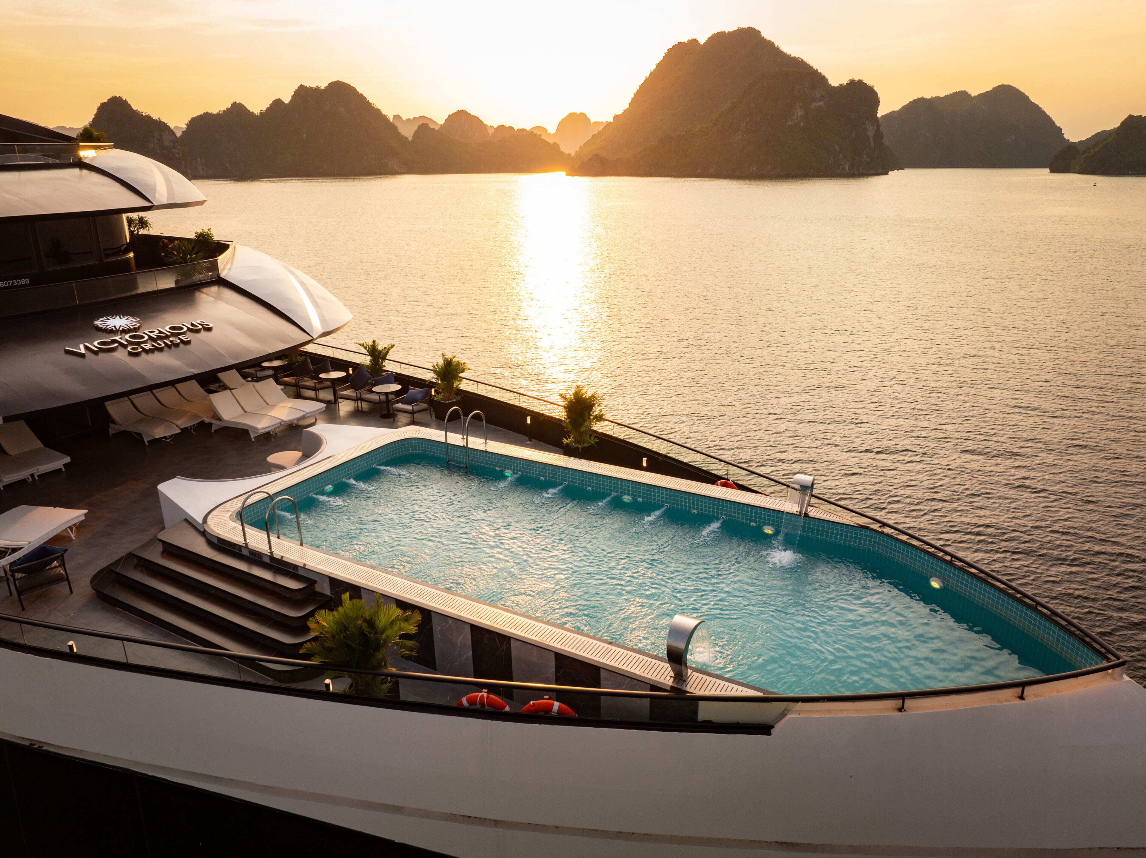 A pool area with lounge chairs and a view of the sea at sunset.
