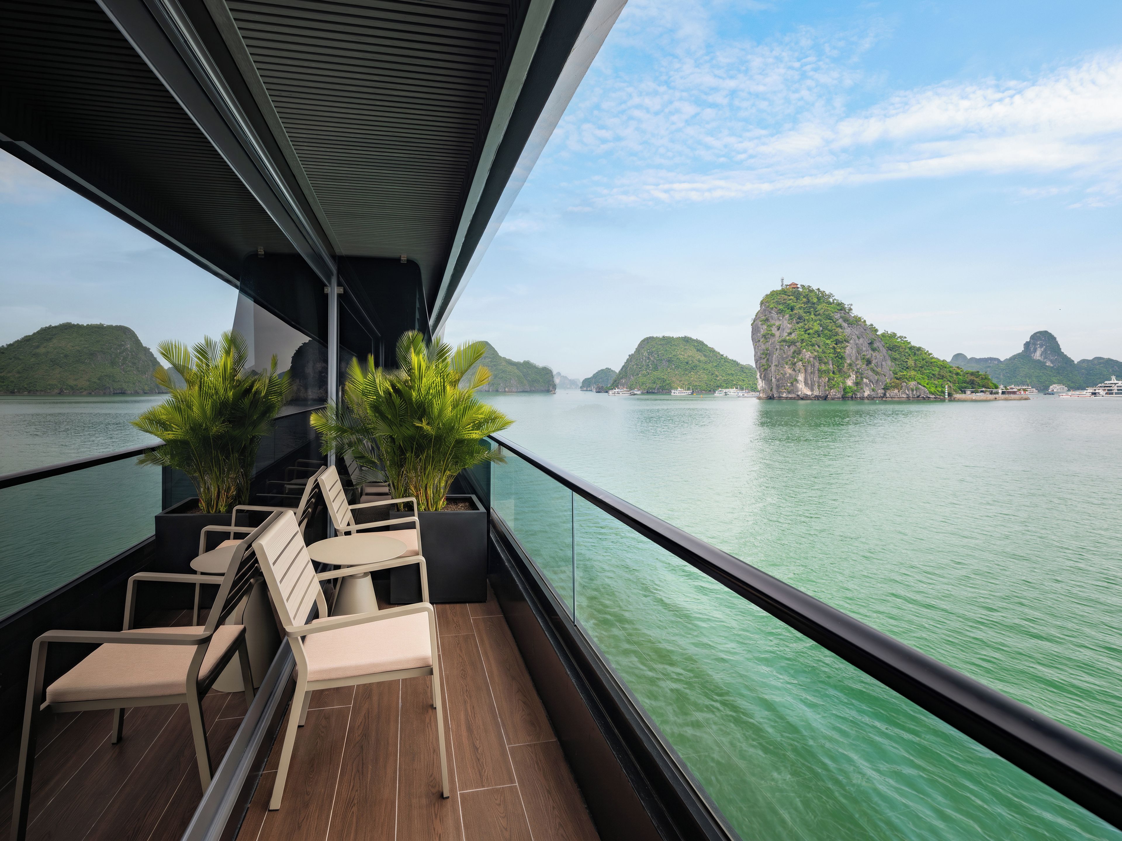 A balcony with chairs and potted plants, overlooking a calm body of water and green islands.