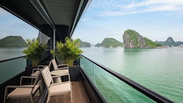 A balcony with chairs and potted plants, overlooking a calm body of water and green islands.