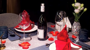 A table set for two with wine glasses, a bottle of wine, a vase with flowers, and red napkins. - Victorious Cruise (Tuan Chau)