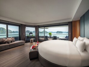 Et moderne soveværelse med en stor seng, et siddeområde, et skrivebord og udsigt til havet.