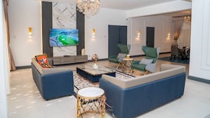 Un soggiorno moderno con un grande televisore, un'area salotto confortevole, un lampadario e una parete in marmo.