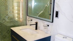Un bagno con lavandino bianco, mobile portaoggetti blu scuro e cabina doccia in vetro.