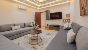 Ett modernt vardagsrum med en grå soffa, ett soffbord och en platt-TV som visar "NETFLIX".
