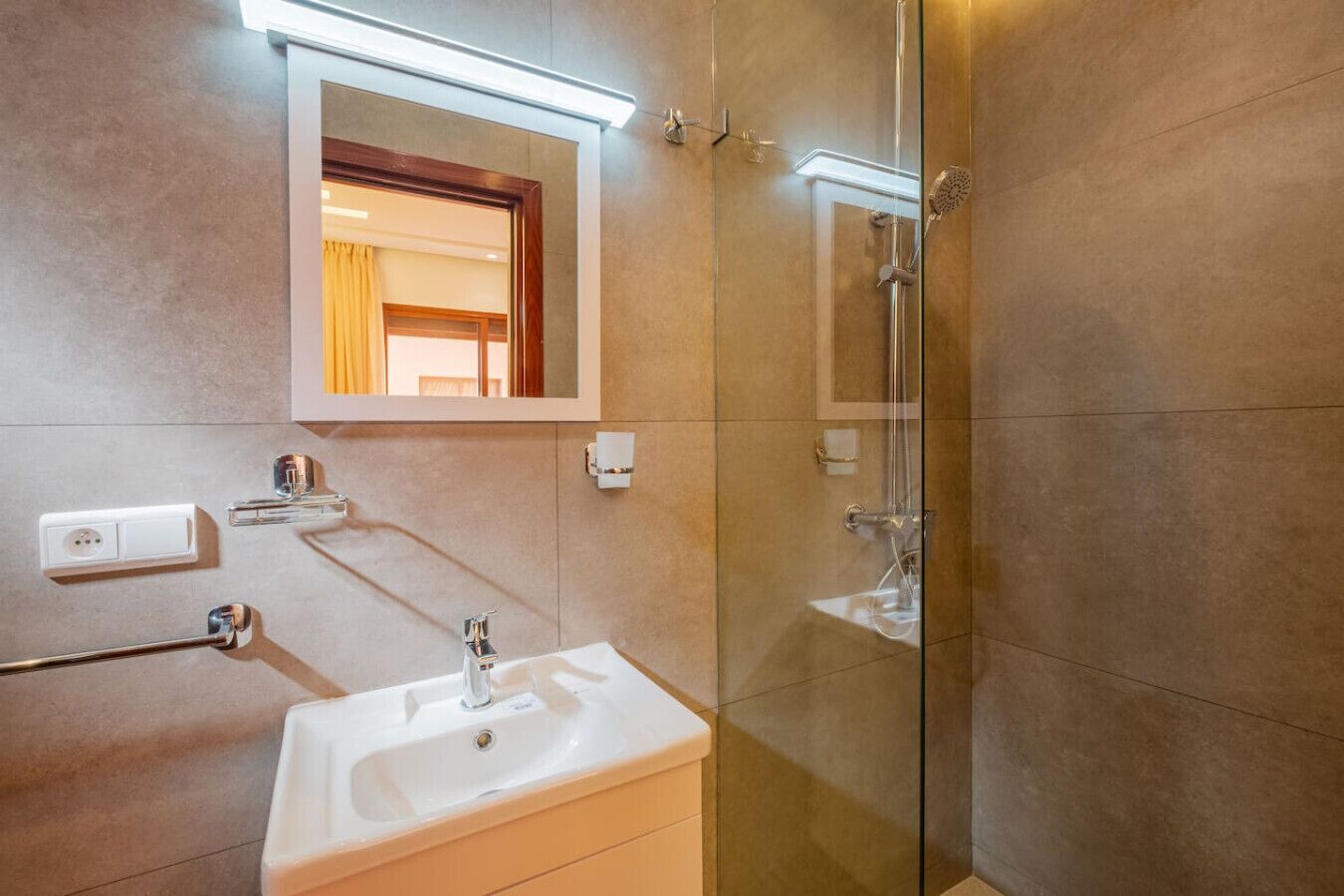 Ein modernes Badezimmer mit Duschkabine aus Glas, einem weißen Waschbecken und einem Spiegel darüber sowie einem Handtuchhalter.