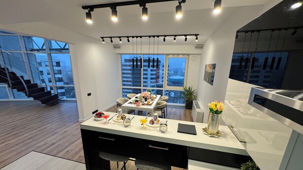 A modern kitchen with a central island, bar stools, and a dining area with a view of the cityscape.