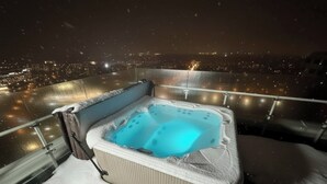 A hot tub on a balcony with a city view at night.