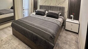 A modern bedroom with a large bed, a nightstand, a mirror, and a marble-patterned wall. - Luxury Apartment- Sahl Hasheesh- Gravity Hotel (Sahl Hasheeh)