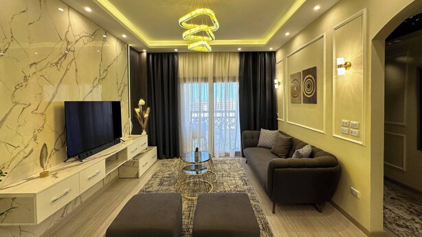 A modern living room with a marble wall, a flat-screen TV, a sofa, and a unique chandelier. - Luxury Apartment- Sahl Hasheesh- Gravity Hotel (Sahl Hasheeh)