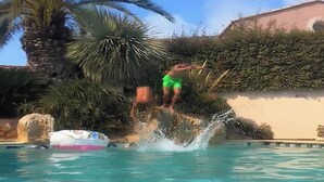 A man in green swim trunks jumping off a rock into a pool. - Beautiful Mediterranean villa with large pool ideal for families (Villeveyrac)