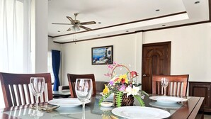 A dining table set for six with a vase of flowers, wooden chairs, and a ceiling fan. - Spacious Corner 1-bedroom Condo With 2 Balconies - Baan Suan (Pattaya)