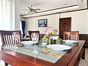 A dining table set for six with a vase of flowers, wooden chairs, and a ceiling fan. - Spacious Corner 1-bedroom Condo With 2 Balconies - Baan Suan (Pattaya)