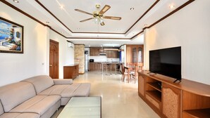 A modern living room with a sofa, a glass coffee table, a TV on a wooden stand, and a ceiling fan. - Spacious Corner 1-bedroom Condo With 2 Balconies - Baan Suan (Pattaya)