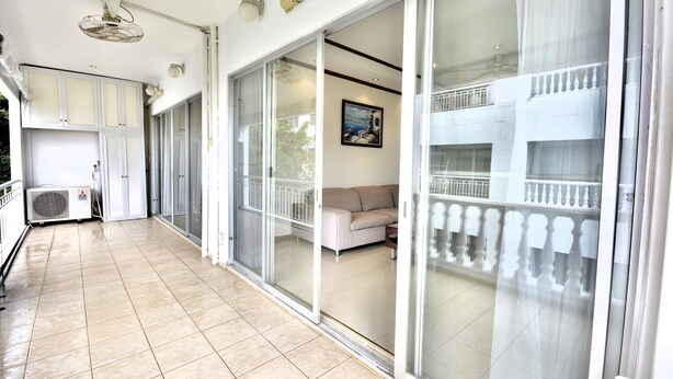A spacious balcony with a sliding glass door leading to a living area, an air conditioning unit, and a ceiling fan. - Spacious Corner 1-bedroom Condo With 2 Balconies - Baan Suan (Pattaya)