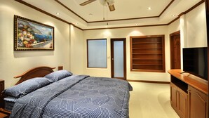 A bedroom with a bed, a ceiling fan, a painting, a television, and a wardrobe. - Spacious Corner 1-bedroom Condo With 2 Balconies - Baan Suan (Pattaya)