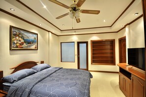 A bedroom with a bed, a ceiling fan, a painting, a television, and a wardrobe. - Spacious Corner 1-bedroom Condo With 2 Balconies - Baan Suan (Pattaya)