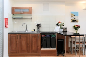 A compact kitchen with wooden cabinets, a sink, a small countertop, and a dining area with chairs. - Quiet One-Bedroom Apartment with Parking (Bath)