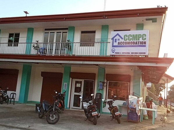 Ein zweistöckiges Gebäude mit einem Schild für CCMPC Accommodation. Vorne sind Motorräder geparkt und eine Person geht auf dem Bürgersteig.