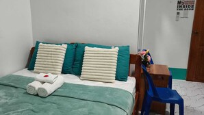 Ein ordentlich gemachtes Bett mit türkisfarbenen und weißen Kissen, einer grünen Decke und zwei aufgerollten Handtüchern.