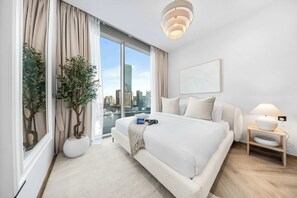 Ein modernes Hotelzimmer mit einem großen Bett, Blick auf die Stadt, einer Zimmerpflanze und einem Nachttisch mit Lampe.