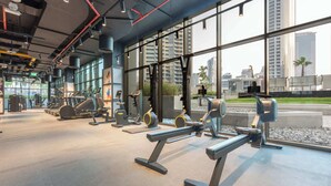 Ett modernt gym med olika typer av träningsutrustning, stora fönster och utsikt över staden.