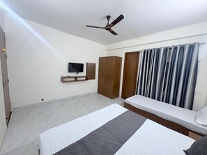 Un dormitorio con una cama, ventilador de techo, televisor, armarios de madera y una ventana con cortinas.