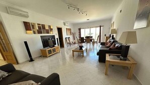 A spacious living room with a black sofa, a TV, a dining area with chairs, and a coffee table. - 🏖 Beach Days, Park Views & Easy Living A Perfect Algarve Family Escape (Silves)