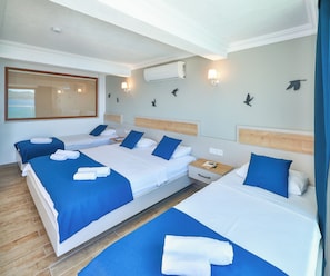A hotel room with three beds, a wooden floor, a window with a view, and wall-mounted air conditioning. - The Kaş Otel (Kas)
