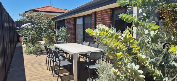 Une terrasse avec une table et des chaises, entourée de plantes et dotée d’une plateforme en bois.