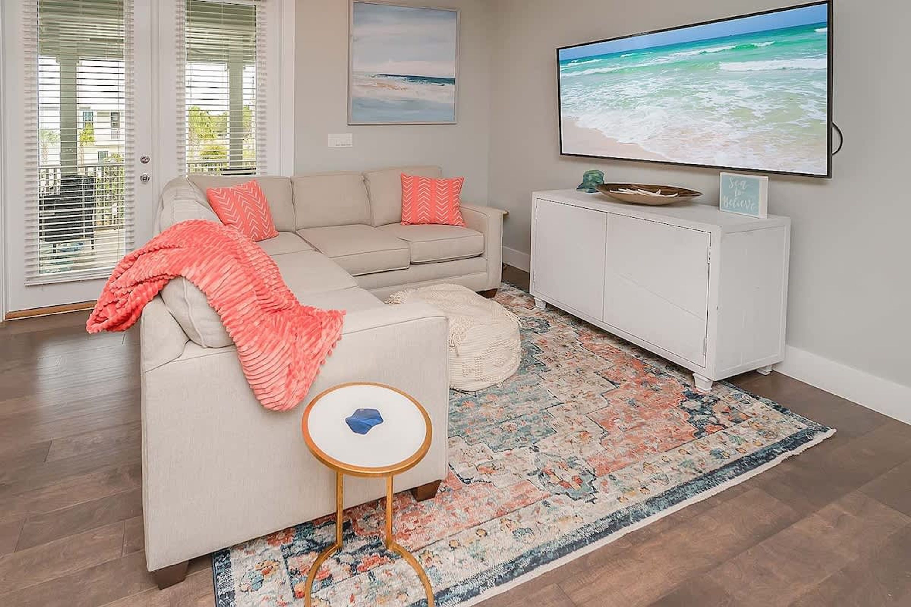 A living room with a beige sofa, a small round table, a patterned rug, a television, and a cabinet.