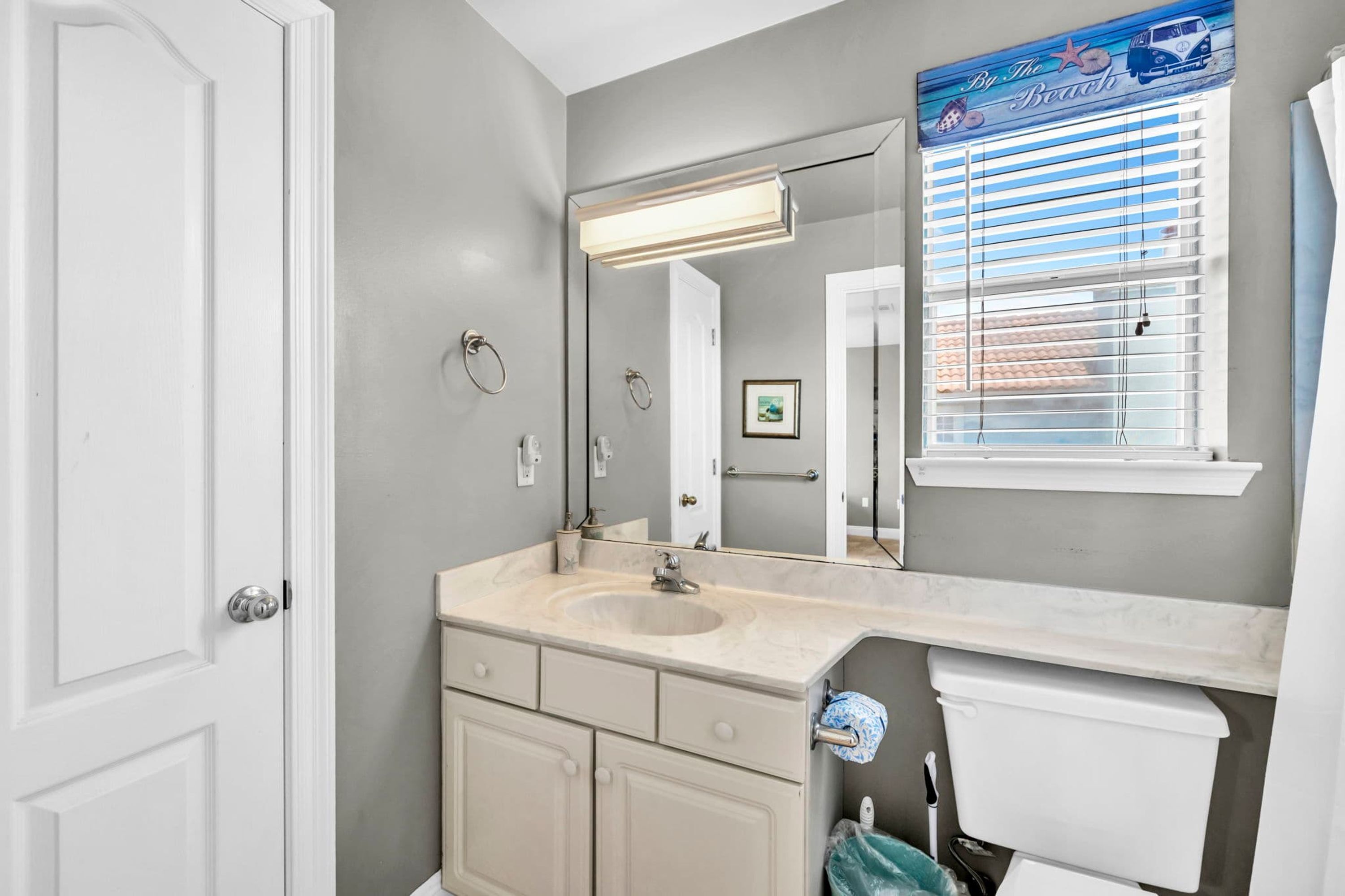 A bathroom with a large mirror, a sink, a toilet, and a window with blinds.