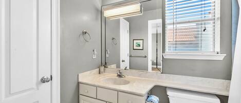 A bathroom with a large mirror, a sink, a toilet, and a window with blinds.