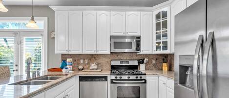 A modern kitchen with white cabinets, stainless steel appliances, and a granite countertop.