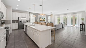 A modern kitchen with white cabinets, stainless steel appliances, and a large island. - Luxury 10br Resort Villa w Pool 10min to Disney (Kissimmee)
