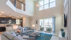 A spacious living area with a high ceiling, a kitchen in the background, and a large window providing natural light. - Superhost Pool Spa Arcade Games - Adventure Villa (Kissimmee)
