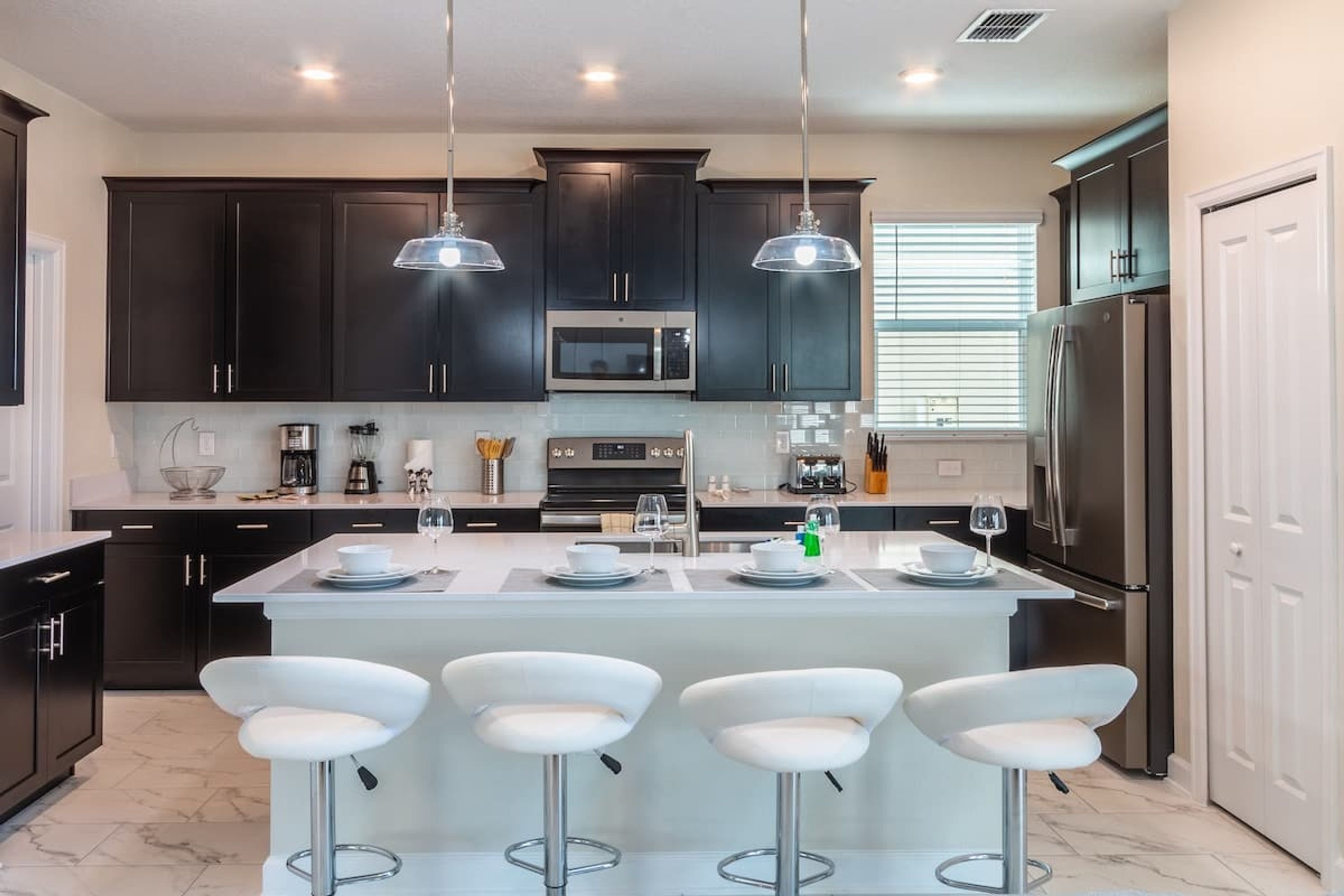 A modern kitchen with dark cabinets, a central island with bar stools, stainless steel appliances, and pendant lighting.