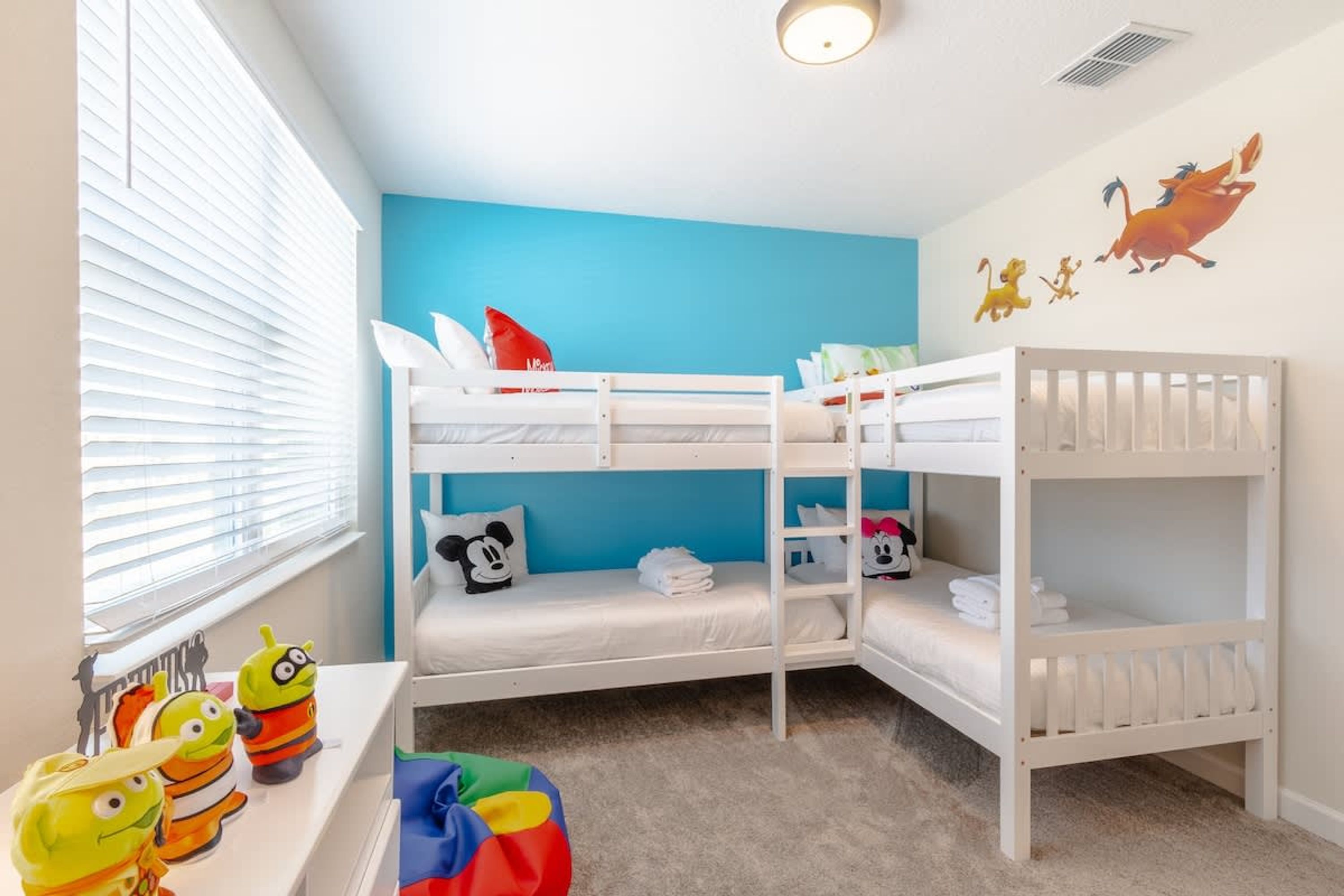 Een slaapkamer met een stapelbed, een blauwe muur, witte beddengoed en een Mickey Mouse kussen.