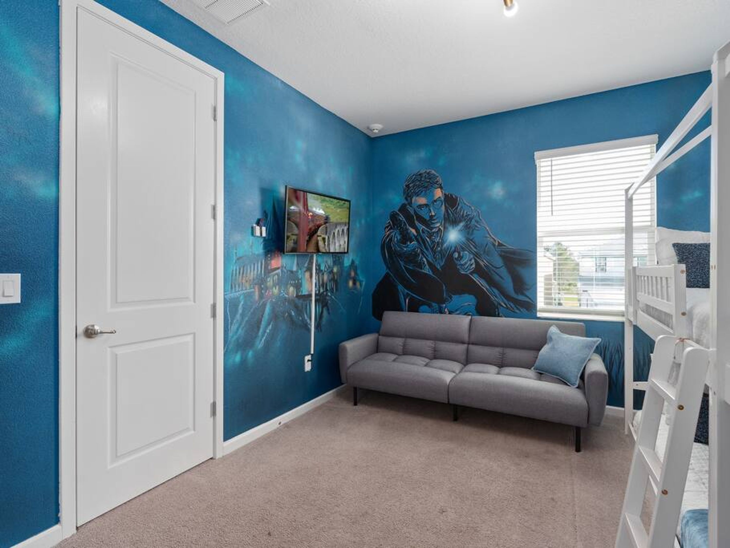 Une pièce avec un mur bleu, un canapé gris, une porte blanche et un lit superposé.