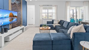 Een moderne woonkamer met een grote flatscreen-tv, een hoekbank, een salontafel en een eethoek met stoelen.