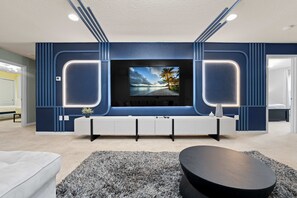 A modern living room with a flat-screen TV mounted on a blue accent wall, a white entertainment unit, and a gray shag rug. - Super Wow- 8bdr-6bas Sick Lake Views (Kissimmee)