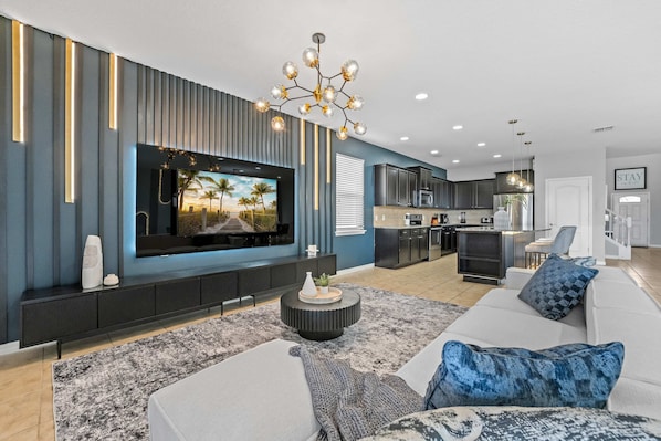 A modern living room with a flat-screen TV, a sofa, a coffee table, and a kitchen in the background. - Super Wow- 8bdr-6bas Sick Lake Views (Kissimmee)