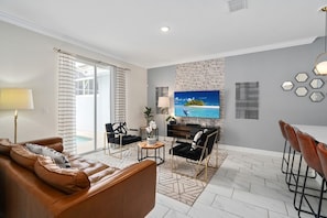 A modern living room with a leather sofa, black chairs, a dining table with chairs, a flat-screen TV, and a large window with a view. - Super Swank - Aesthetic Designs Amenities (Davenport)