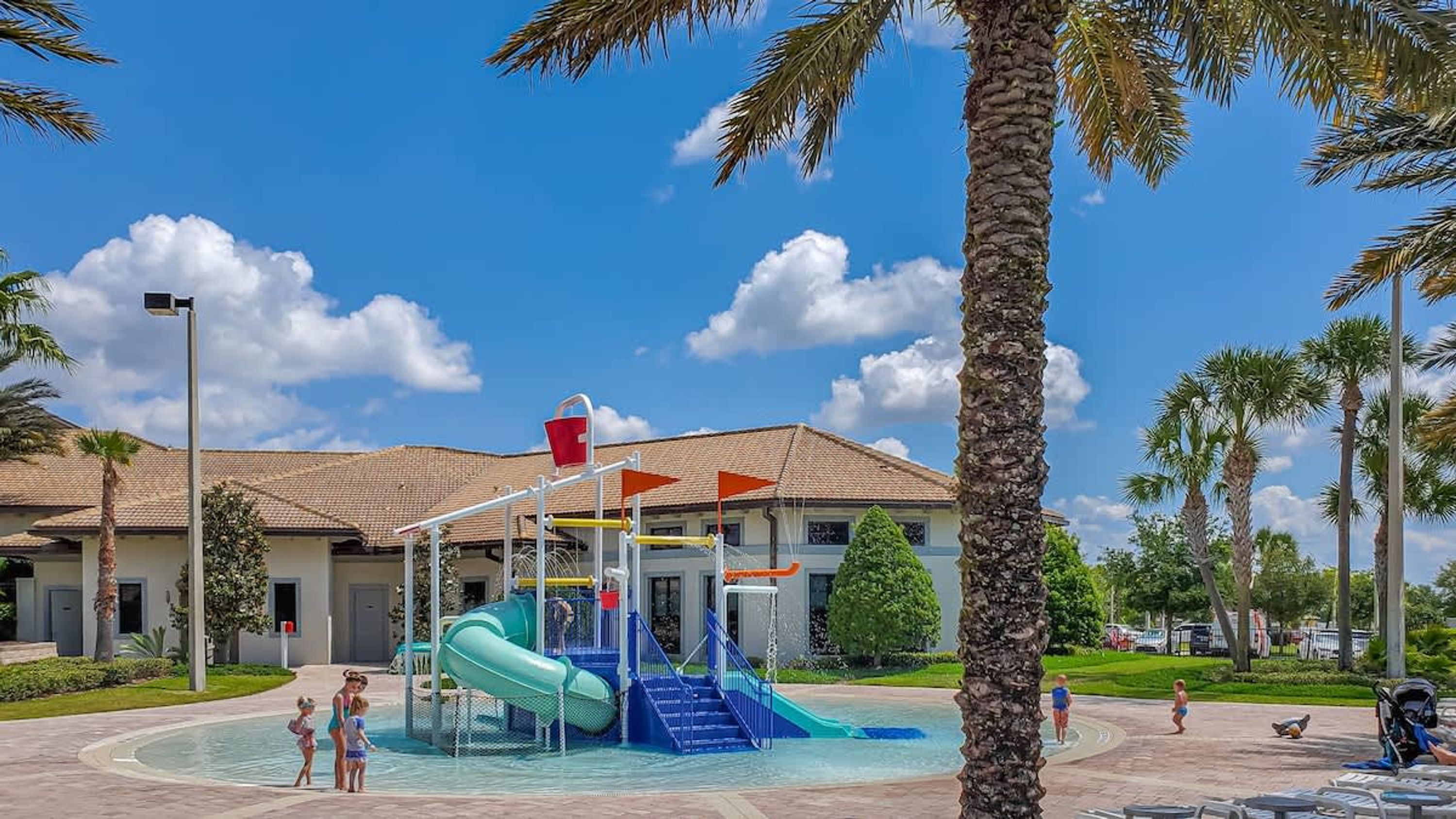 A water park with a blue slide, a red bucket, and palm trees.