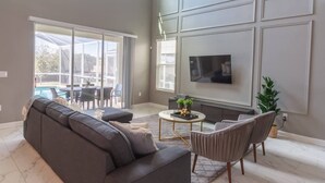 A modern living room with a grey sofa, a coffee table, and a TV mounted on the wall. - Comfortable Beds - Fully Equipped Kitchen Pool Spa (Kissimmee)