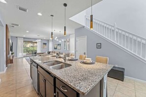 A modern kitchen with granite countertops, a central island, and a dining area with a staircase. - Ultimate 6BR Fun Pool Table Movie Games (Kissimmee)