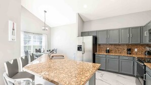 A modern kitchen with granite countertops, grey cabinets, and stainless steel appliances. - Sunny Escape Swim Play (Kissimmee)