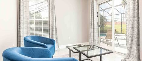 A modern living room with a blue sofa, a glass coffee table, and large sliding glass doors leading to a patio area.