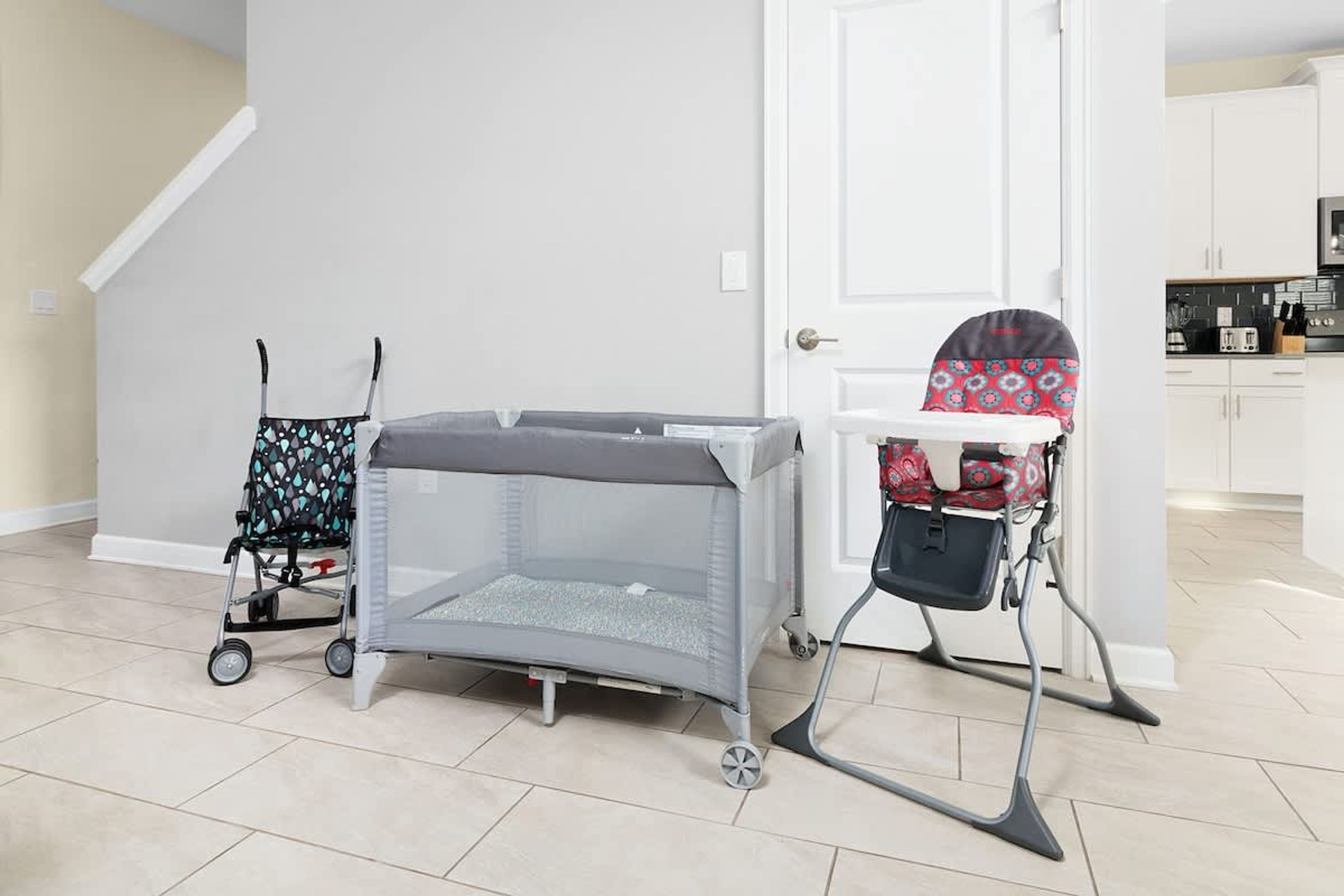 A room with a baby playpen, a stroller, and a high chair.