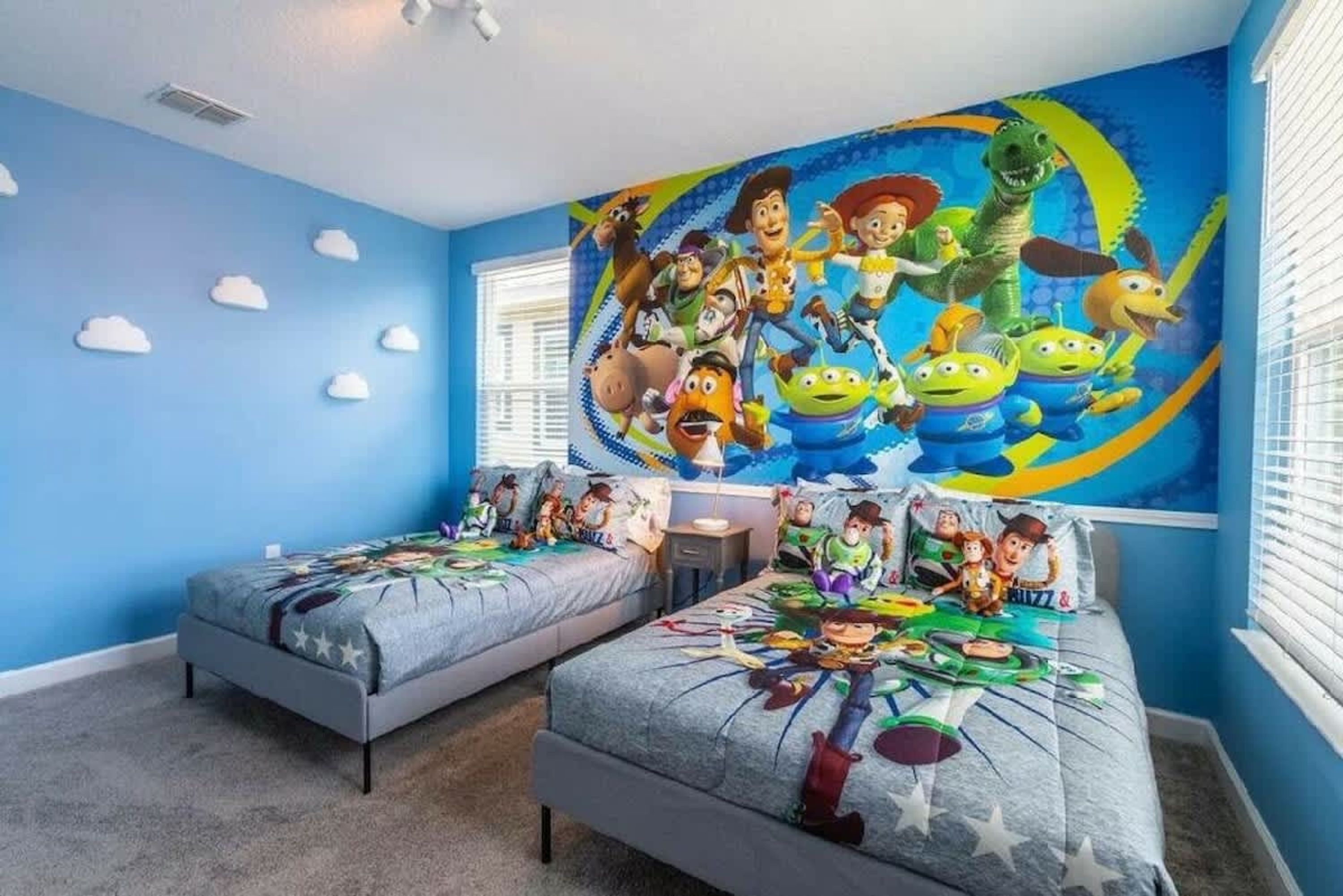 Ein Schlafzimmer mit zwei Betten, einer Wandmalerei mit animierten Figuren und einem Fenster mit Jalousien.